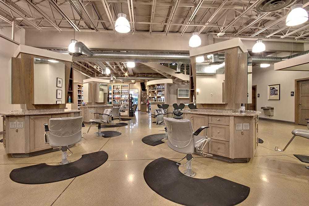 Modern hair salon interior with styling stations and chairs, neutral tones, overhead lighting.