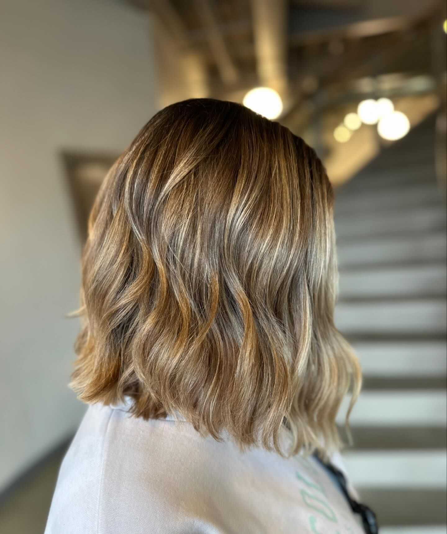 Wavy, shoulder-length hair with subtle blonde highlights in a softly lit setting.