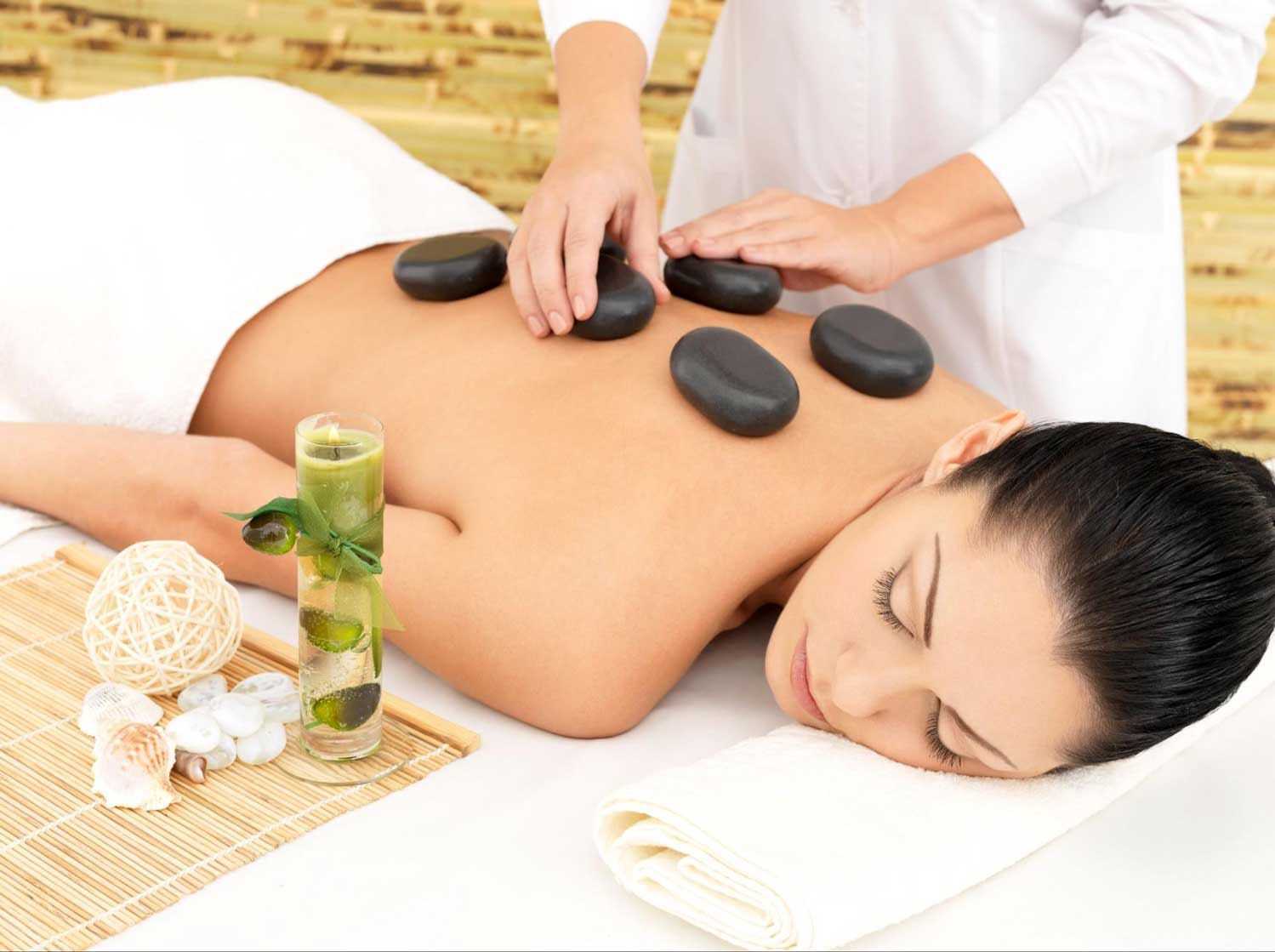 Woman receiving a hot stone massage at a spa with a relaxing setup.