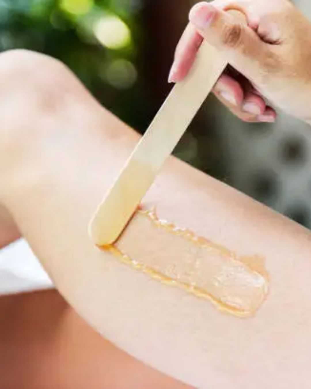 Applying wax with a wooden spatula on a person's leg for hair removal.