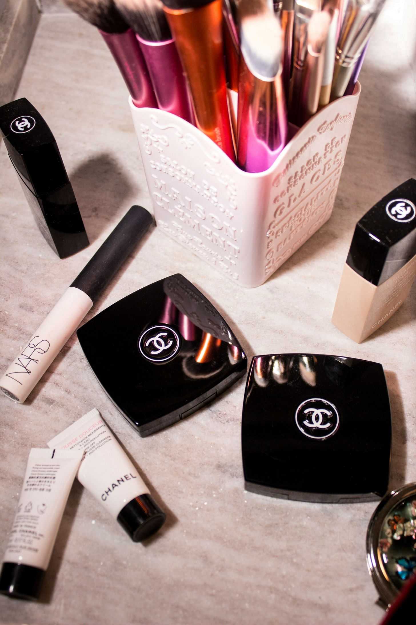 Makeup collection displayed on a marble surface with brushes in a container.