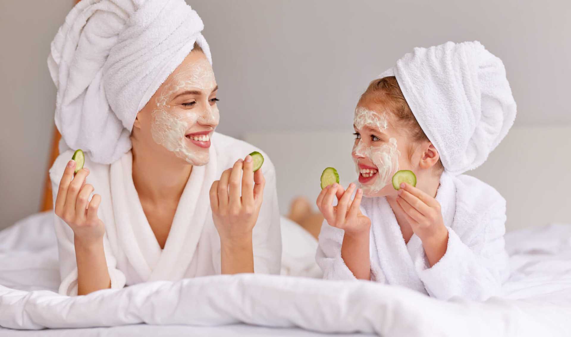 Mother and child enjoying spa day with face masks and cucumber slices.