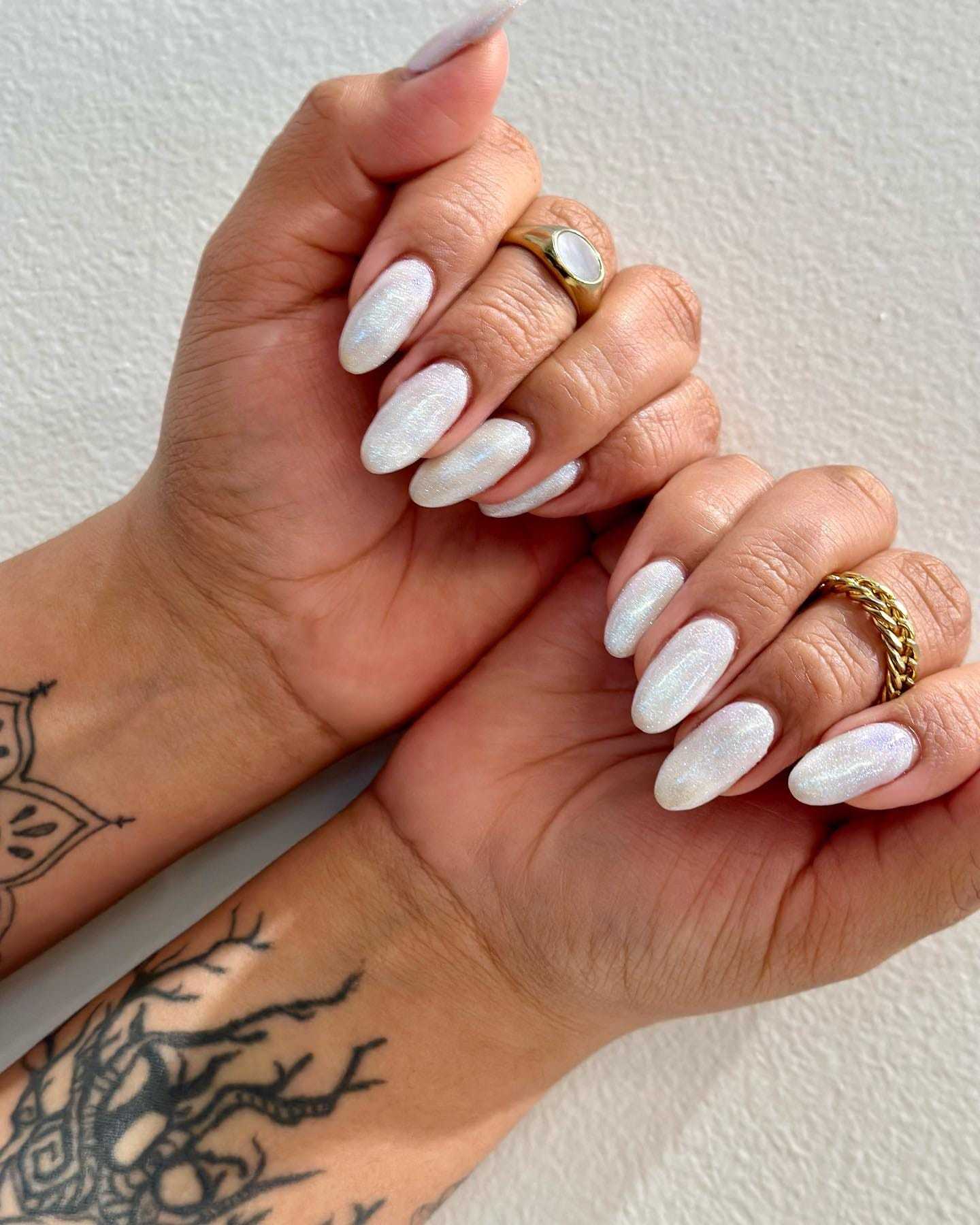 Tattooed hands with shimmering white manicured nails and gold rings.