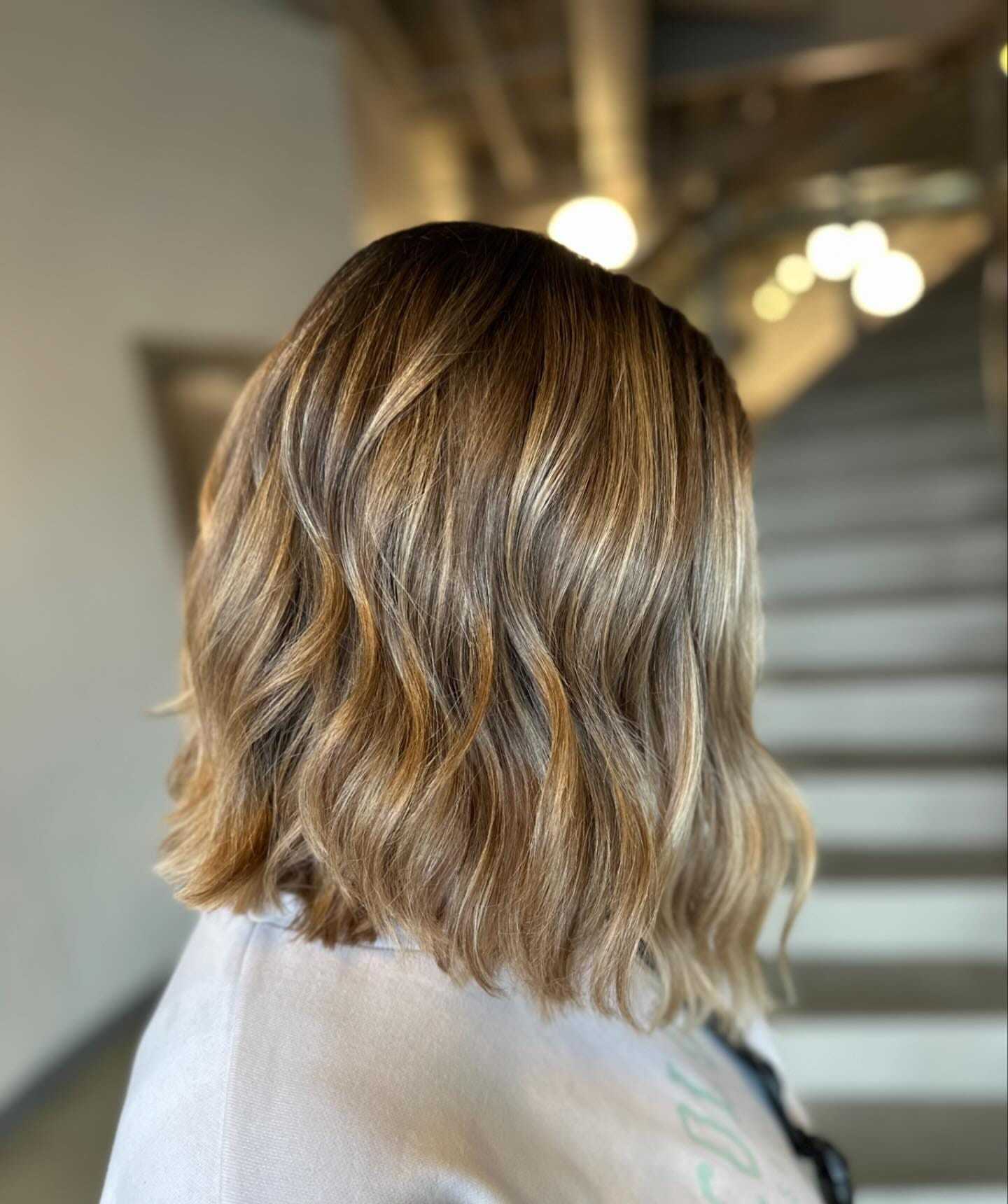 Wavy, shoulder-length hair with subtle blonde highlights in a softly lit setting.