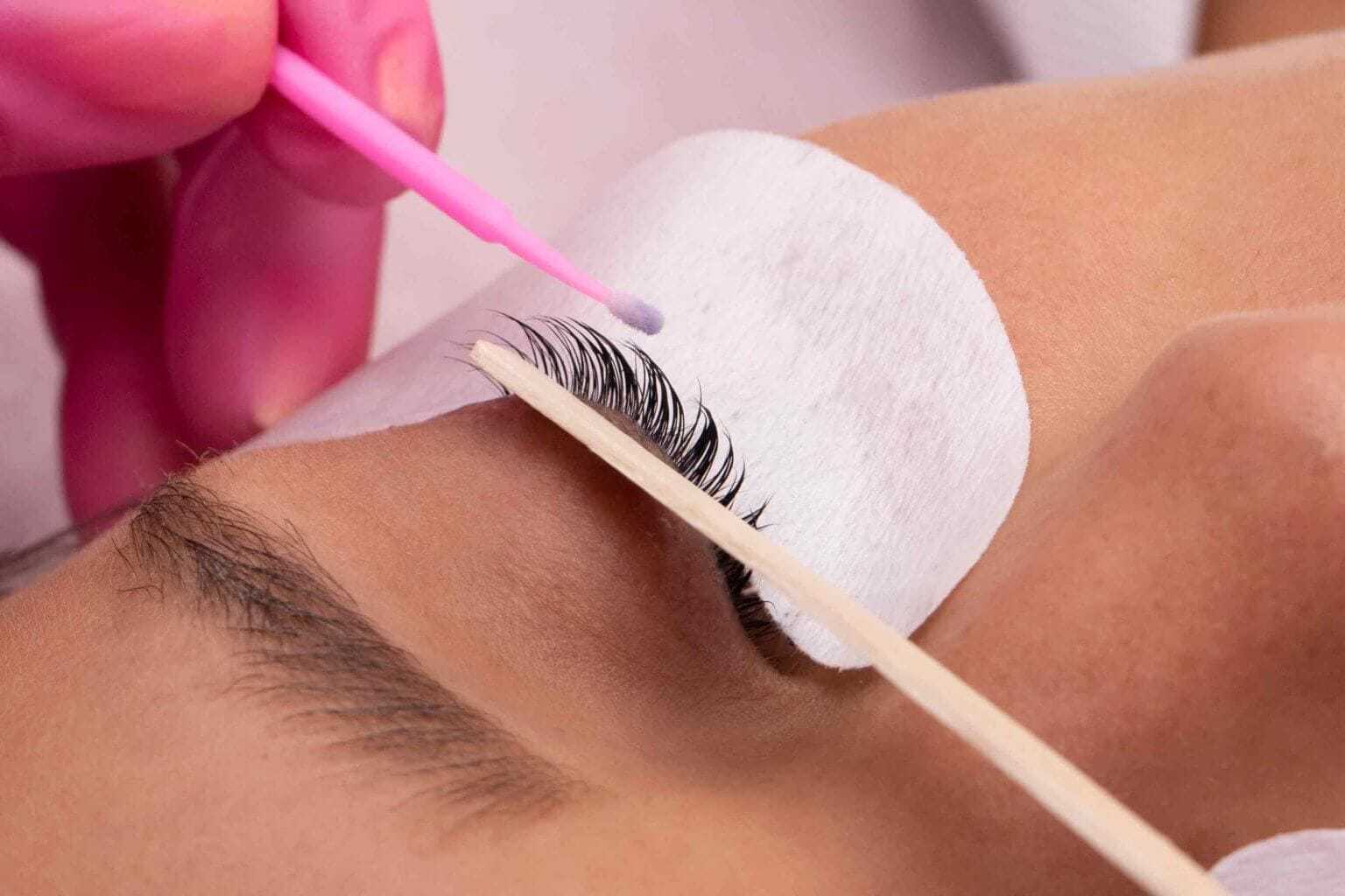 Eyelash extension application on a closed eye with protective pads and tools.