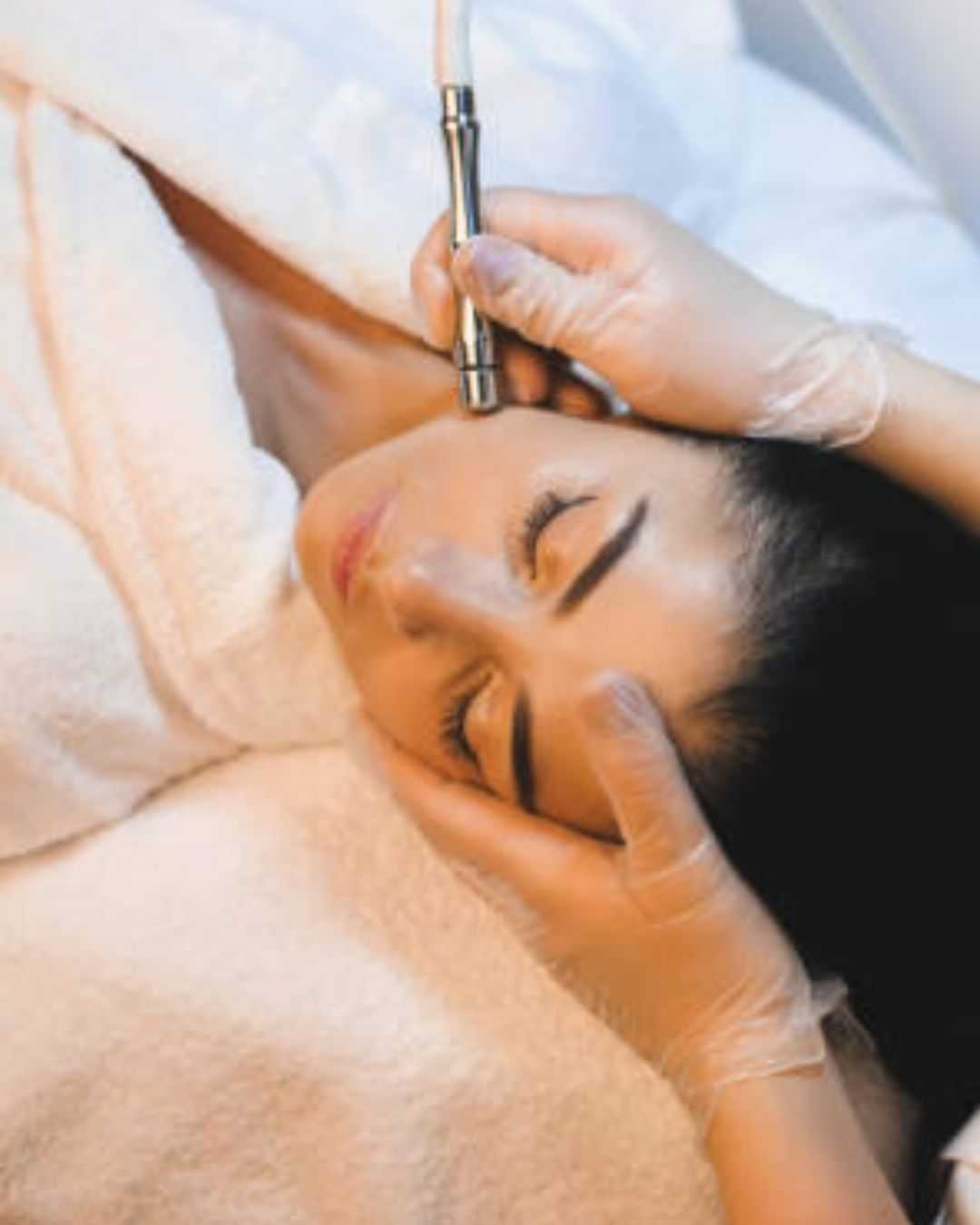 Woman receiving a facial treatment with a handheld device in a spa setting.