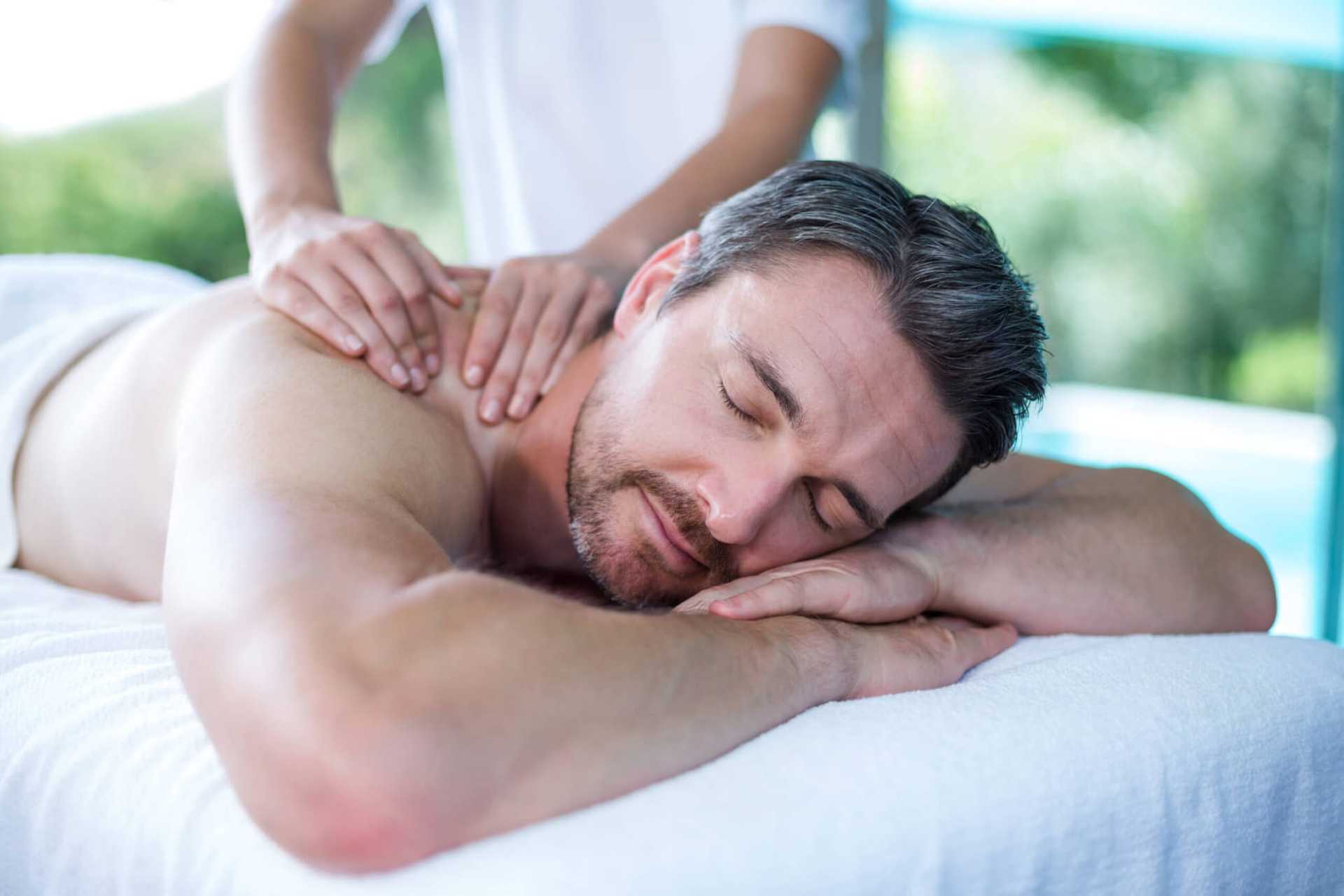 Man receiving a relaxing back massage, lying on a white towel with eyes closed.
