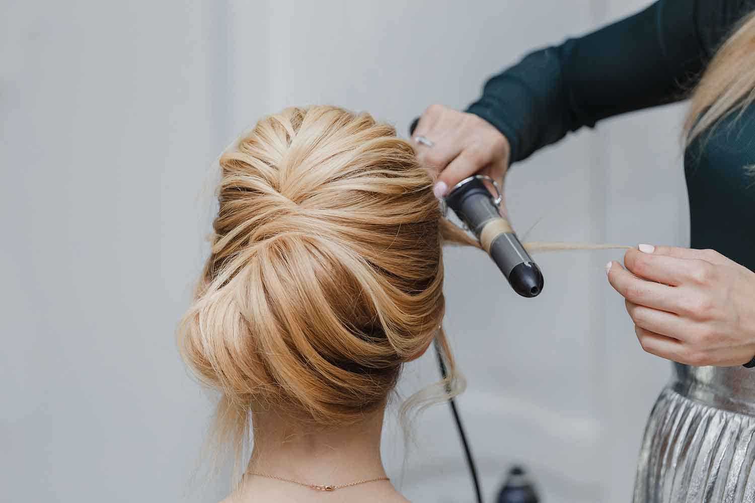 Hairdresser styling blonde hair with a curling iron.