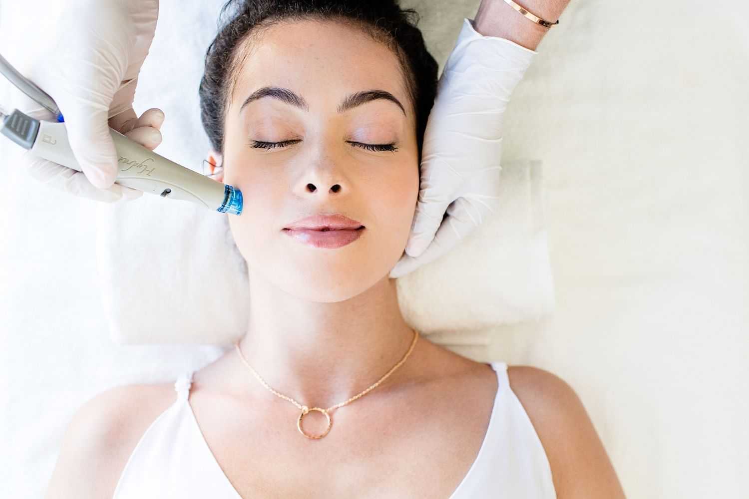 Woman receiving facial treatment with beauty device, eyes closed and relaxed.